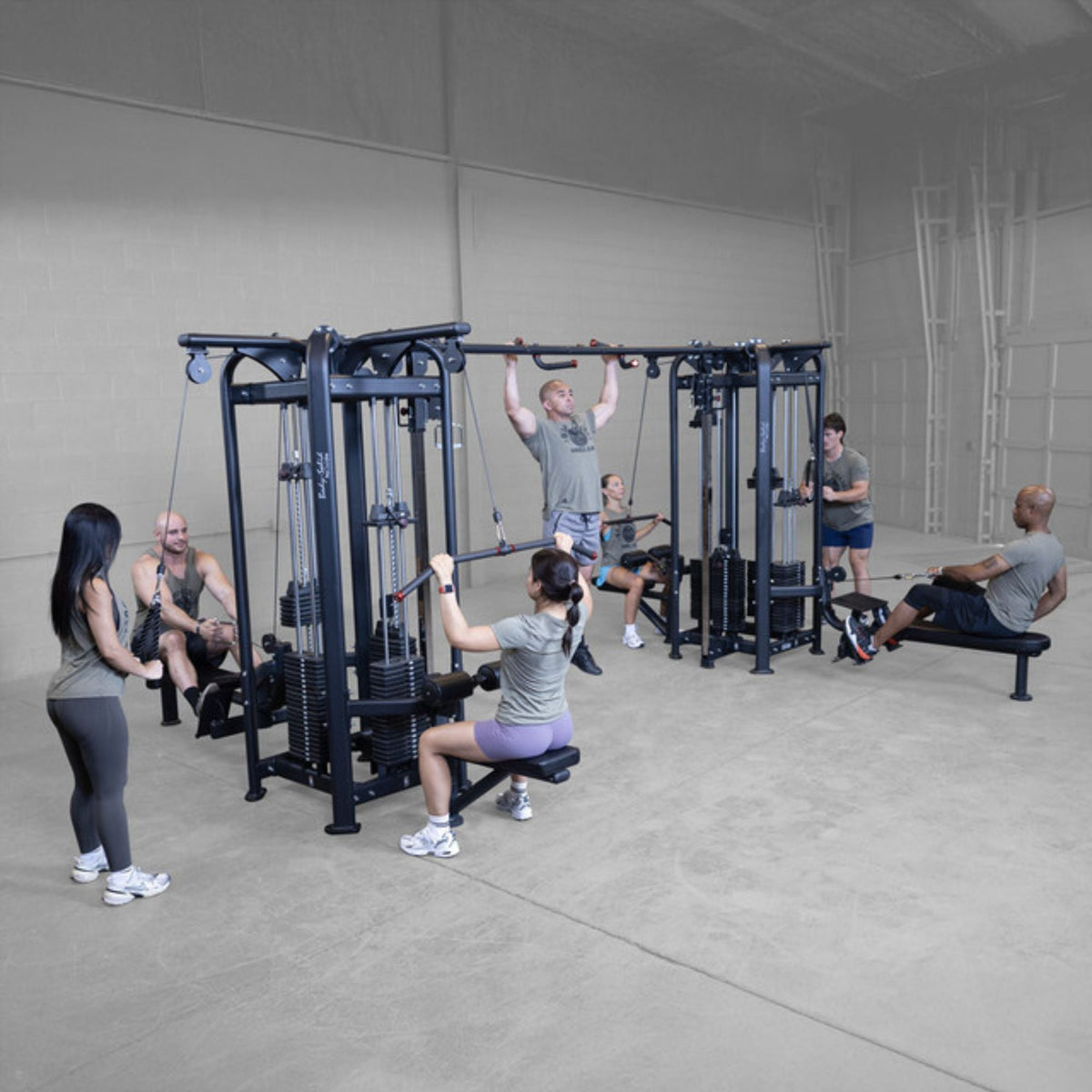 Body-Solid Pro ClubLine SJG Jungle Gym SJG800 Group of people working out on multi-station cable gym performing lat pulldowns, pull-ups, and seated rows in a spacious gym.