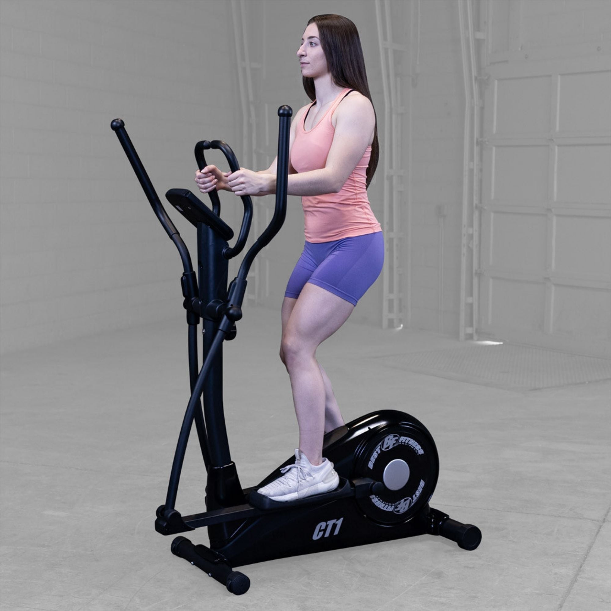 Best Fitness Cross Trainer Elliptical BFCT1B Three-quarter view of woman training on Best Fitness CT1 elliptical trainer in a gray gym setting.

