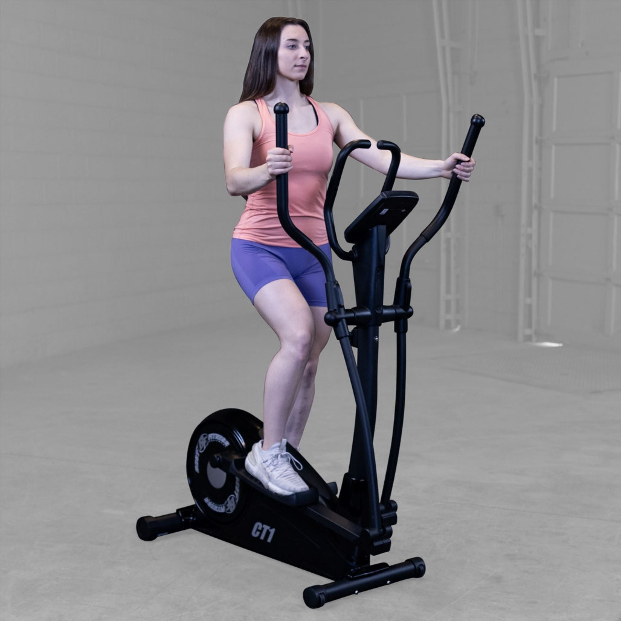Best Fitness Cross Trainer Elliptical BFCT1B Woman in coral top and purple shorts using Best Fitness CT1 elliptical for indoor cardio exercise.

