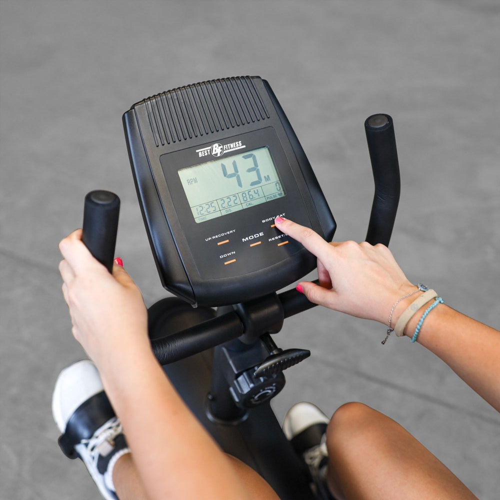 Best Fitness Recumbent Bike BFRB1B Close-up view of a person using the Best Fitness RB1 recumbent bike console, adjusting workout settings on the digital display.