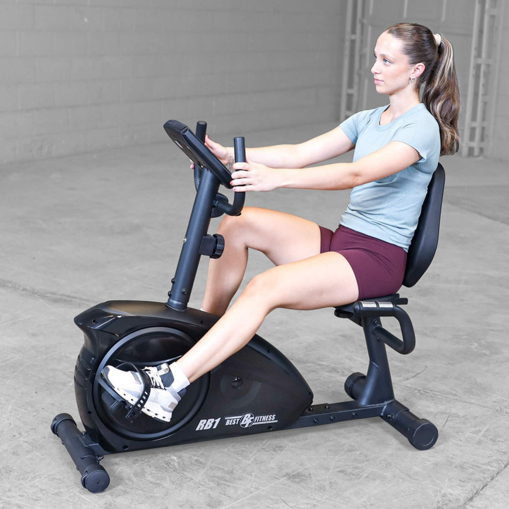 Best Fitness Recumbent Bike BFRB1B Female model seated on Best Fitness RB1 recumbent bike holding handlebars while cycling indoors.