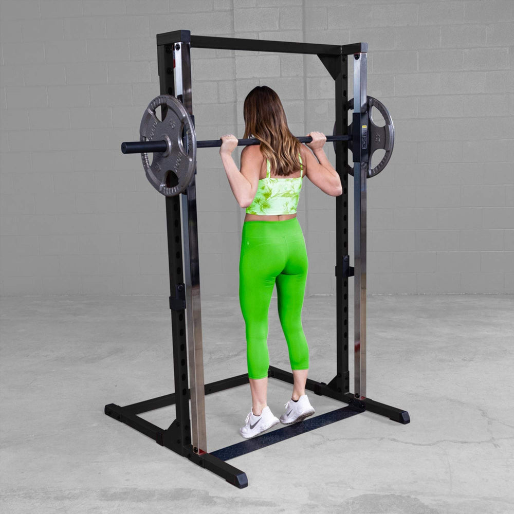 Best Fitness Smith Machine BFSM250B Back view of woman holding barbell at shoulder height inside Body-Solid Smith machine frame