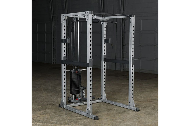 A Body-Solid GPR378 Power Rack with lat cable pulley gym machine with a safety guard and weight stack, photographed in a garage setting with a concrete floor and dark garage door background.