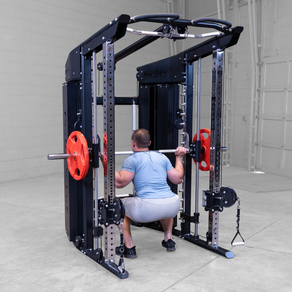 A man performing a squat on a Body-Solid-GSFR-100All-in-OneFunctional-Trainer-Smith-Machine with red weight plates in a garage setting.