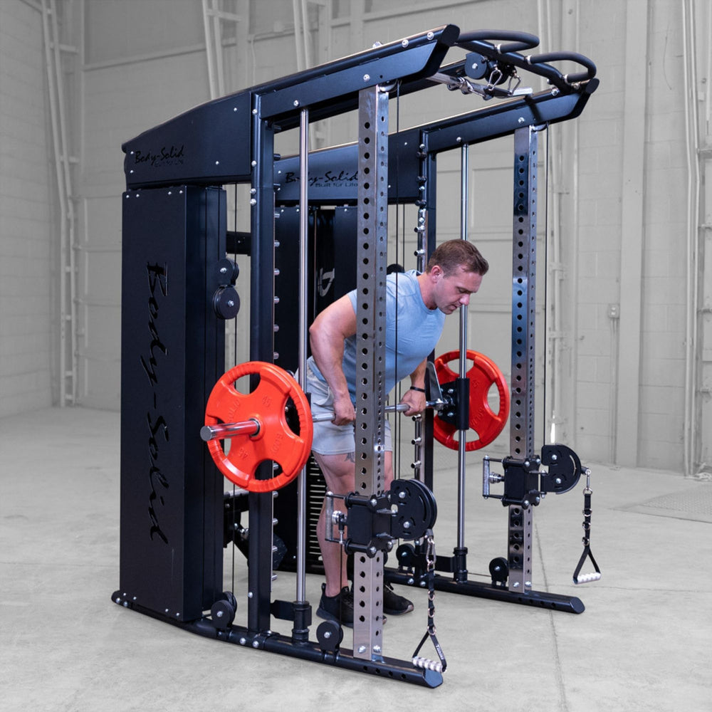 A man in a light blue t-shirt and gray shorts performs a cable push-up on a Body-Solid-GSFR-100All-in-OneFunctional-Trainer-Smith-Machine with red weight plates, set in a warehouse gym environment.