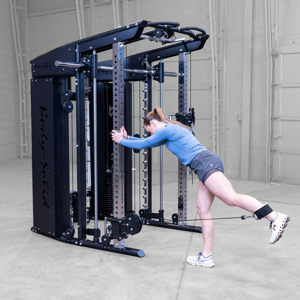 A woman exercises with a cable attachment on a black Body-Solid-GSFR-100All-in-OneFunctional-Trainer-Smith-Machine dual-functional gym machine in a warehouse gym setting.
