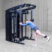 A woman exercises with a cable attachment on a black Body-Solid-GSFR-100All-in-OneFunctional-Trainer-Smith-Machine dual-functional gym machine in a warehouse gym setting.