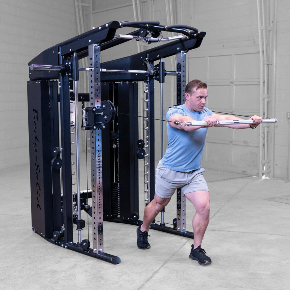 A man in a blue t-shirt and gray shorts performs a cable pull-through exercise on a Body-Solid-GSFR-100All-in-OneFunctional-Trainer-Smith-Machine