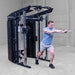 A man in a blue t-shirt and gray shorts performs a cable pull-through exercise on a Body-Solid-GSFR-100All-in-OneFunctional-Trainer-Smith-Machine