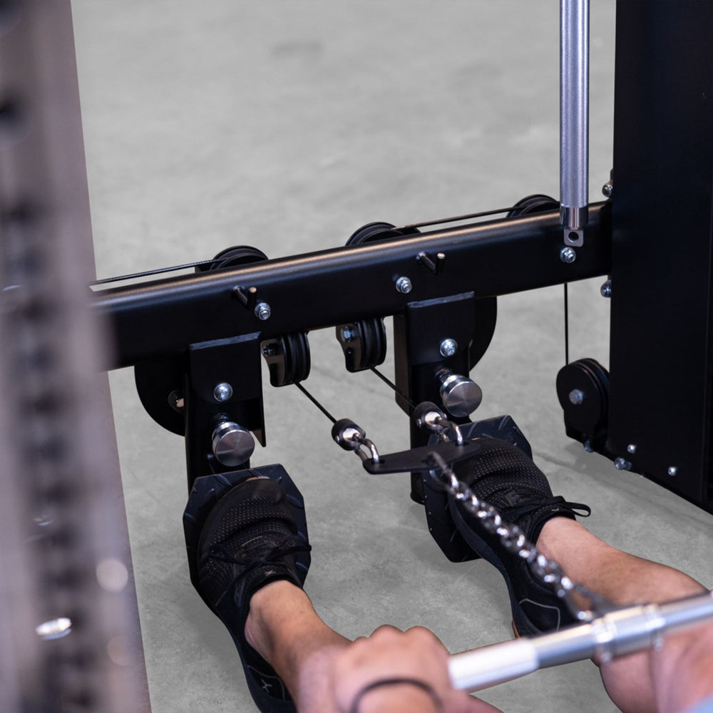 Close-up of a person using a cable pulley on a Body-Solid-GSFR-100All-in-OneFunctional-Trainer-Smith-Machine  in a gym, with their feet resting on footrests and hands pulling a bar with a chain attachment.