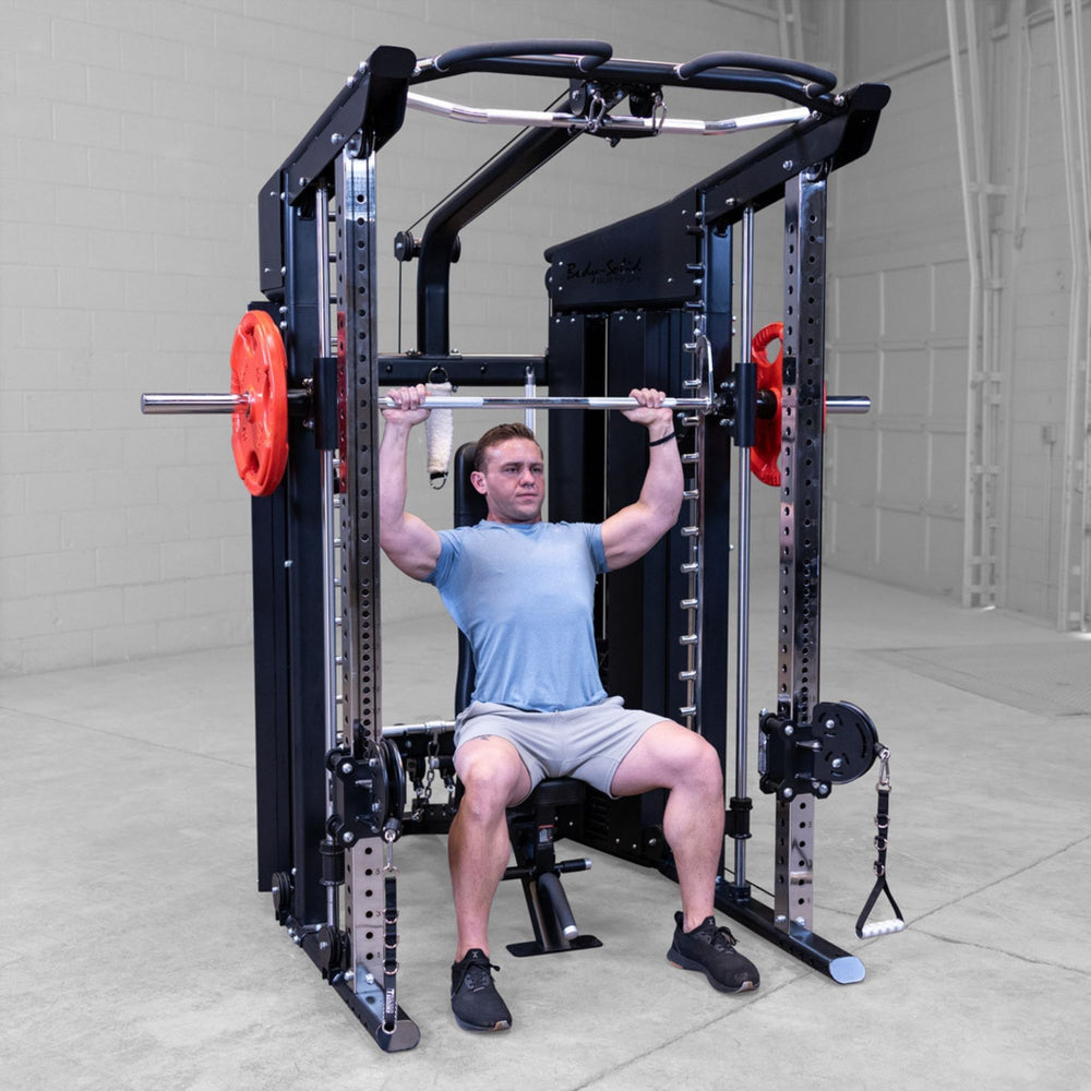 A man performing a barbell squat on a Body-Solid-GSFR-100All-in-OneFunctional-Trainer-Smith-Machine in a concrete-floored indoor gym space.