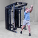 A man in a gym using a dual cable pulley system attached to a Body-Solid-GSFR-100All-in-OneFunctional-Trainer-Smith-Machine, wearing a light blue t-shirt, gray shorts, and black sneakers.