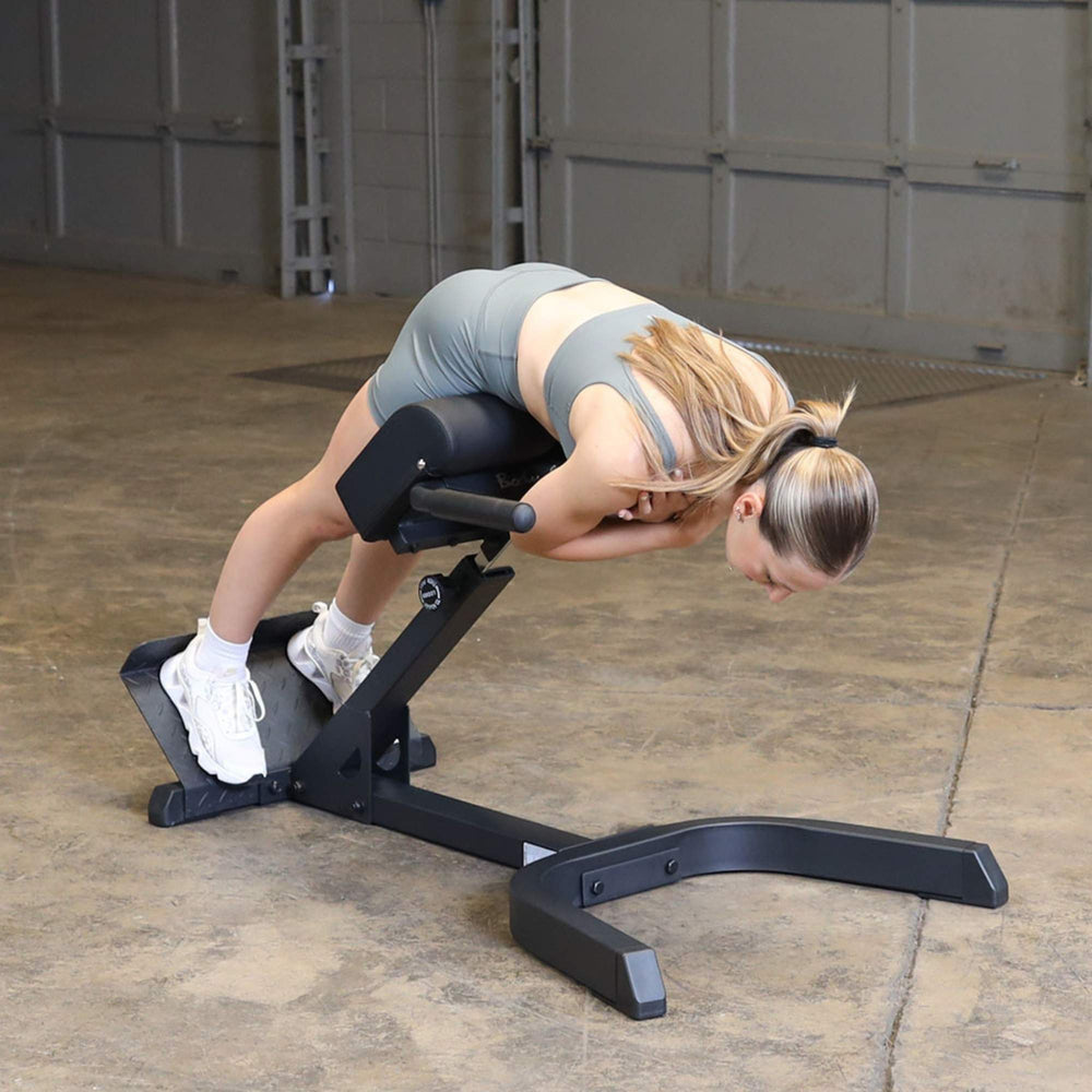 Body-Solid 45 Back Hyperextension GHYP345B Woman bent forward mid-back extension on hyperextension machine.