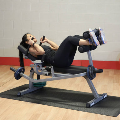 Body-Solid Ab Crunch Machine GAB100B Woman performing weighted ab crunch on  abdominal bench in gym setting