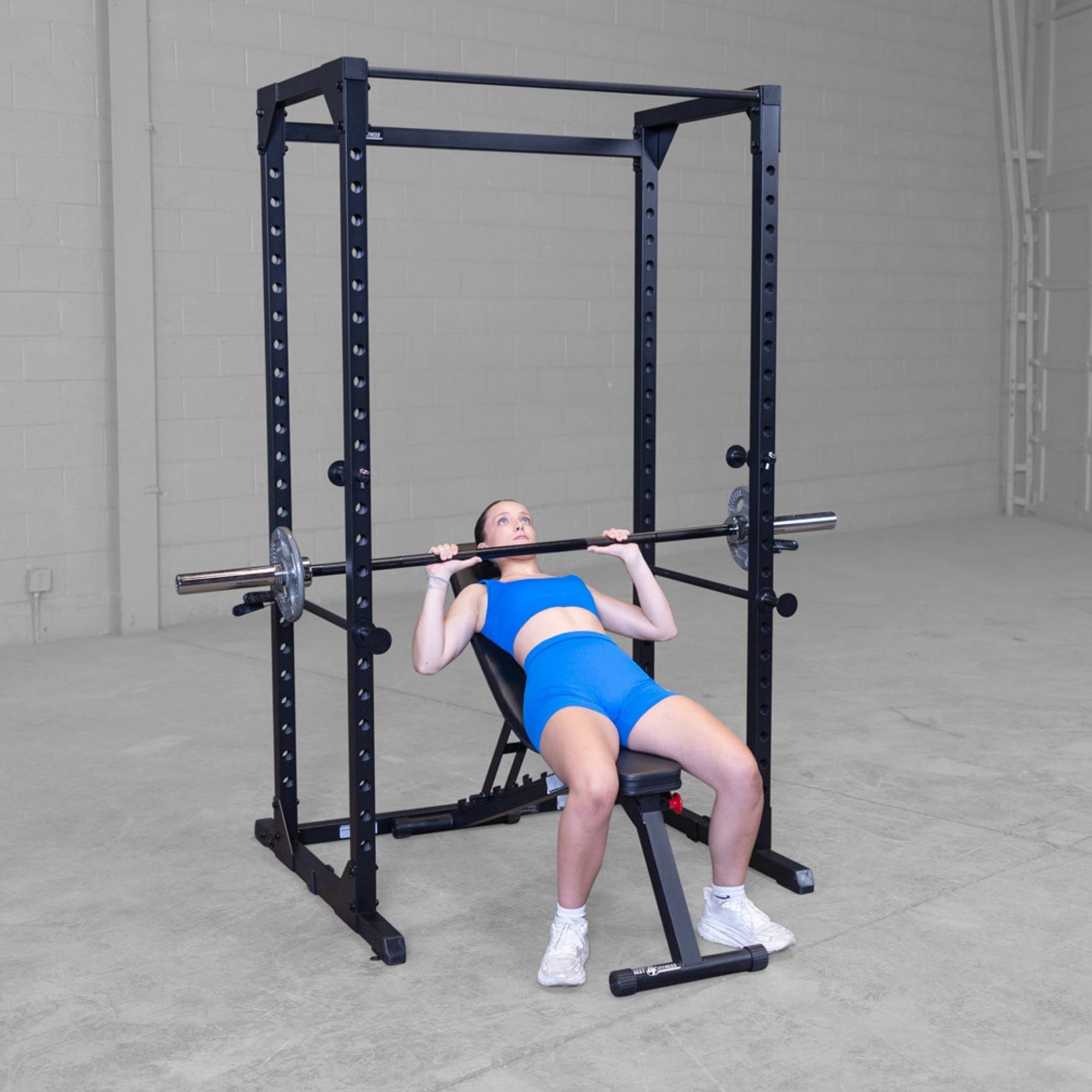 Body-Solid Best Fitness Power Rack BFPR100B Woman lying on adjustable bench performing an incline bench press inside a power rack.
