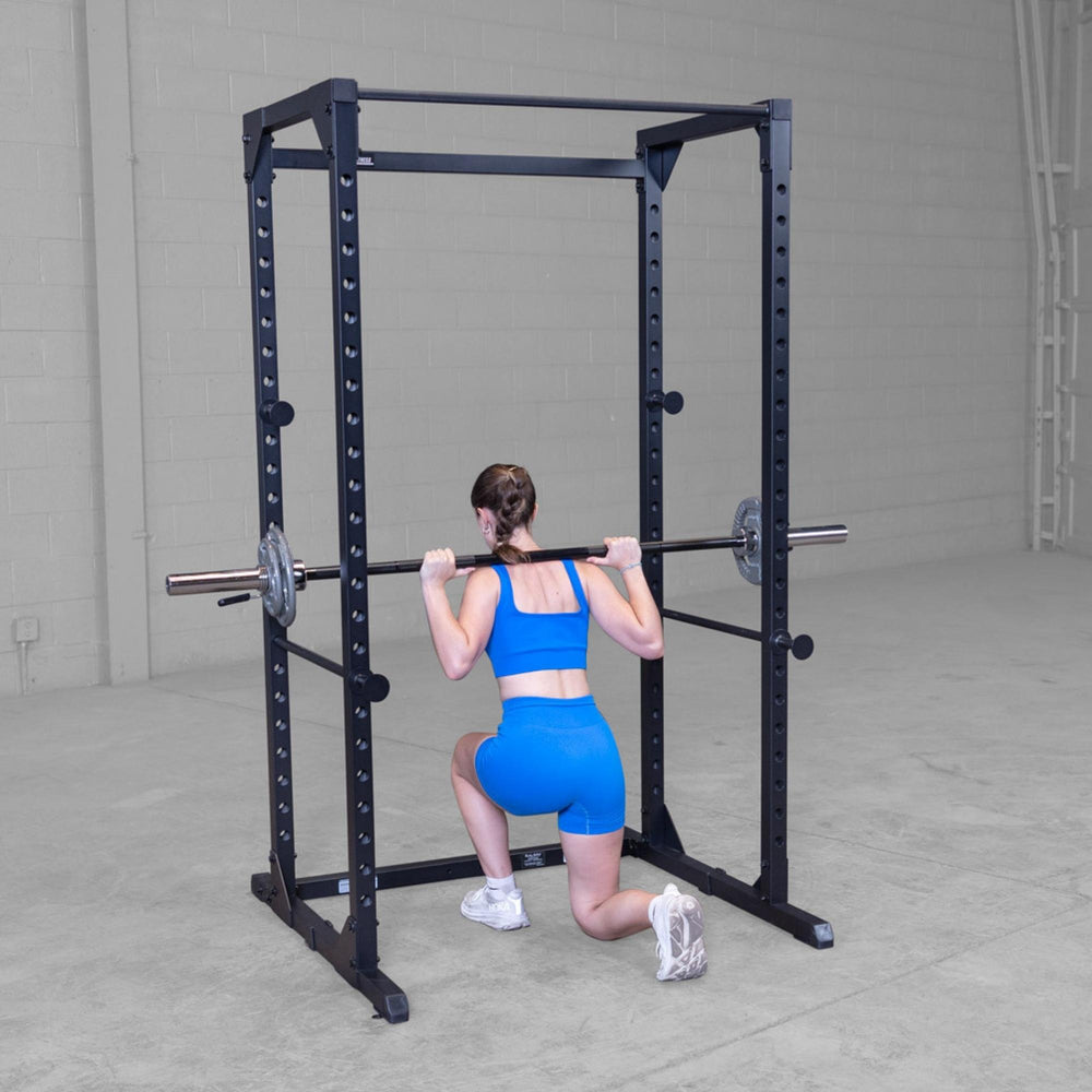 Body-Solid Best Fitness Power Rack BFPR100B Woman doing barbell lunges inside a black power rack in a bright gym.
