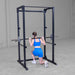 Body-Solid Best Fitness Power Rack BFPR100B Woman doing barbell lunges inside a black power rack in a bright gym.
