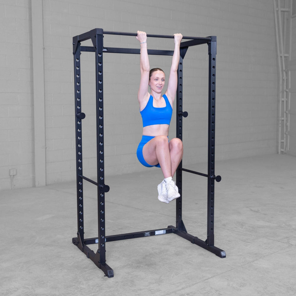 Body-Solid Best Fitness Power Rack BFPR100B Woman hanging from power rack performing a hanging leg raise exercise.
