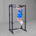 Body-Solid Best Fitness Power Rack BFPR100B Woman performing a pull-up using the top bar of a power rack in a minimalist gym.

