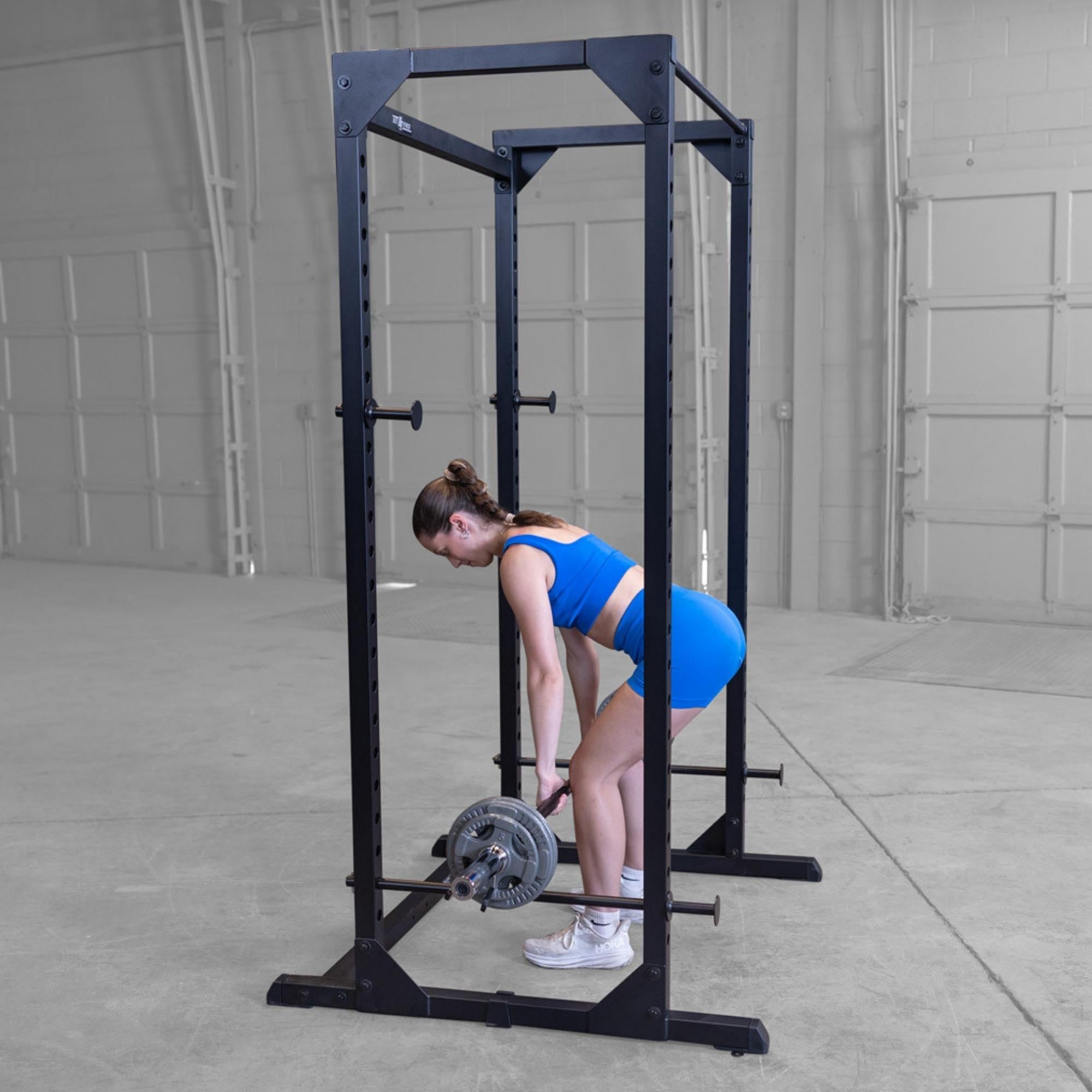 Body-Solid Best Fitness Power Rack BFPR100B Woman performing barbell deadlifts inside a black power rack with neutral background.

