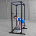 Body-Solid Best Fitness Power Rack BFPR100B Woman performing barbell deadlifts inside a black power rack with neutral background.
