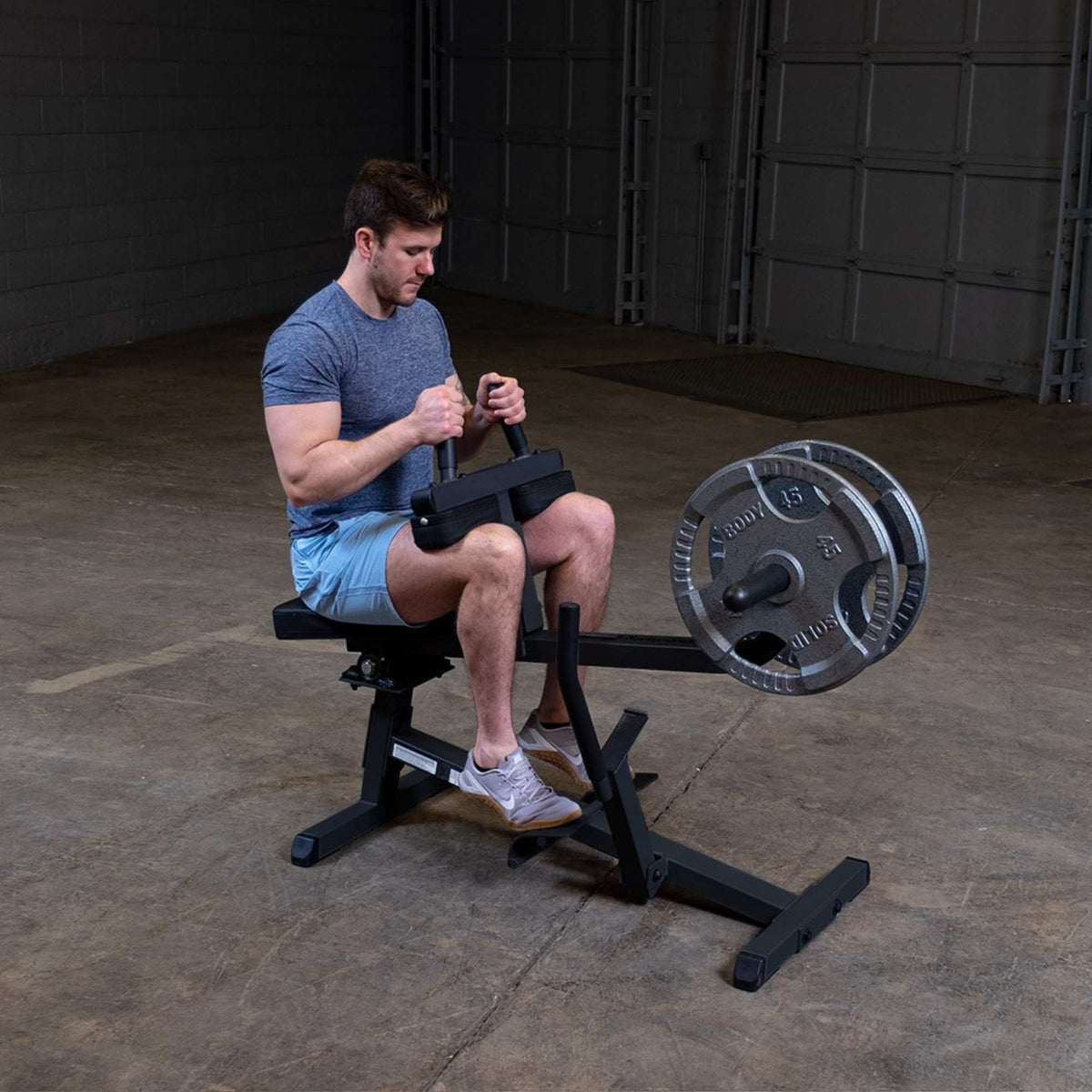 Body-Solid Commercial Seated Calf Raise GSCR349B Man using  seated calf raise machine loaded with silver weight plates in a gym