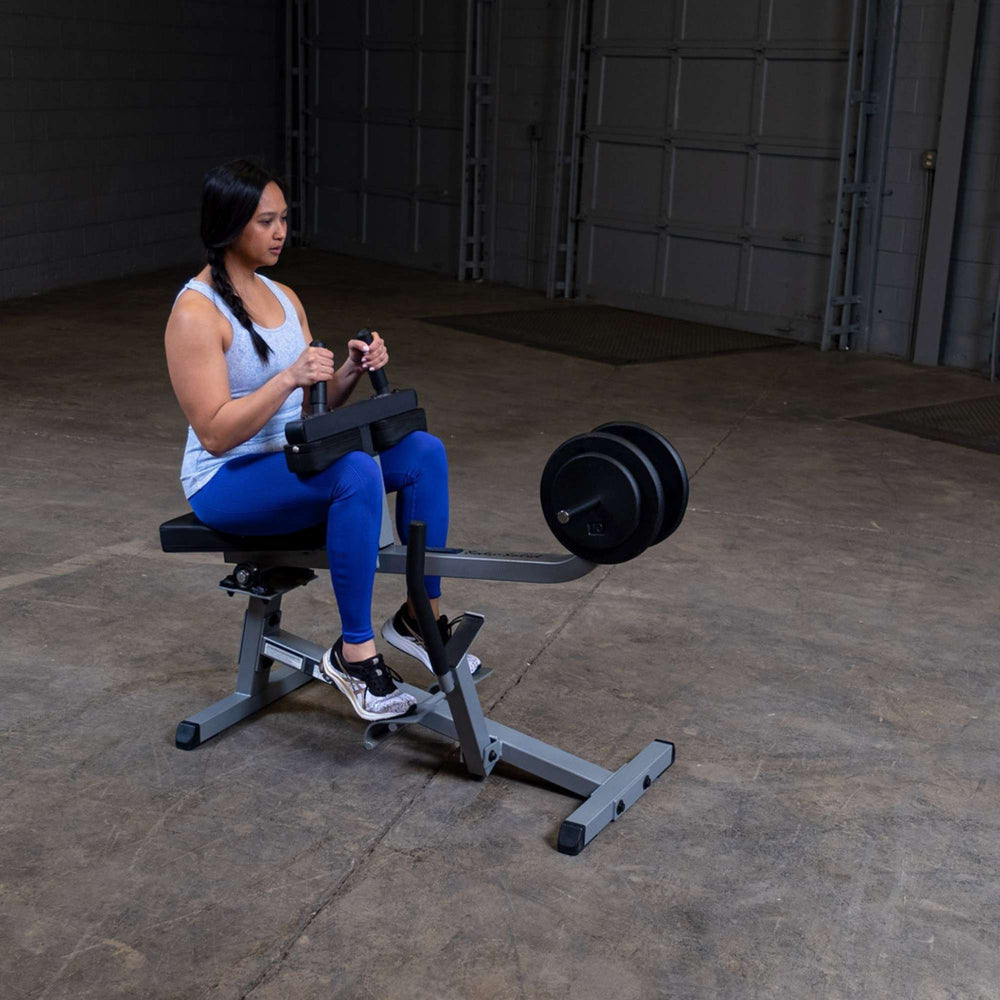 Body-Solid Commercial Seated Calf Raise GSCR349B Woman in blue leggings using  calf raise machine with black bumper plates