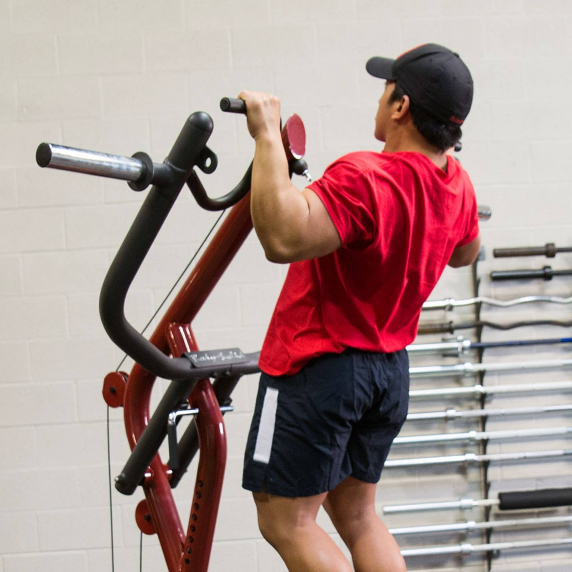 Body-Solid Corner Leverage Gym GLGS100B Athlete doing pull-ups on a red multi-functional gym station, lifting his body using overhead bars.
