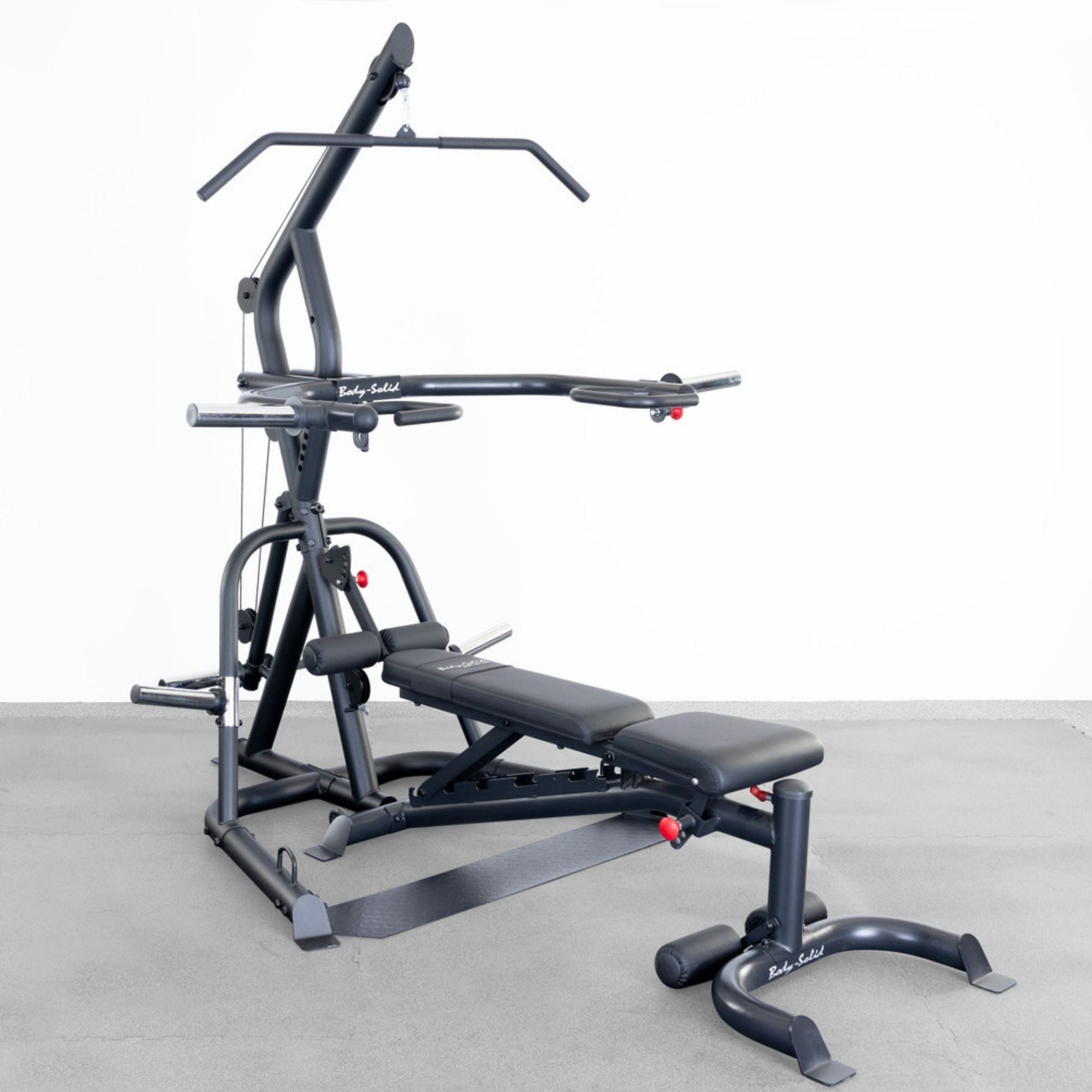 Body-Solid Corner Leverage Gym GLGS100B Multi-function gym station with adjustable bench, lat pulldown bar, and dual press arms, set on a concrete floor.
