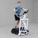 Body-Solid Endurance Center Drive Elliptical E100 Man exercising on Endurance E100 elliptical trainer, demonstrating full stride motion in industrial gym space.

