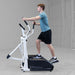 Body-Solid Endurance Center Drive Elliptical E100 Man using Endurance E100 elliptical trainer with hands on moving handles during cardio workout session.
