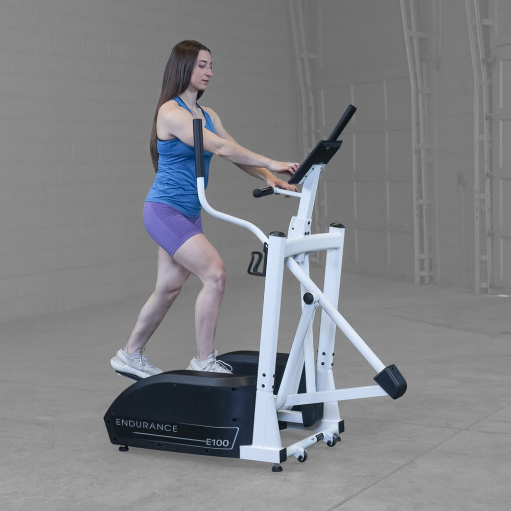 Body-Solid Endurance Center Drive Elliptical E100 Profile view of woman striding on Endurance E100 elliptical trainer, demonstrating smooth motion and posture alignment.