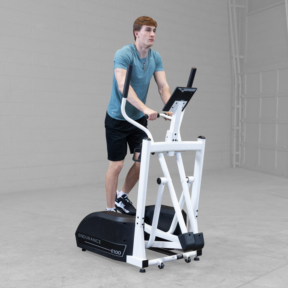Body-Solid Endurance Center Drive Elliptical E100 Side view of man performing cardio workout on Endurance E100 elliptical machine, showing stride motion and balance.
