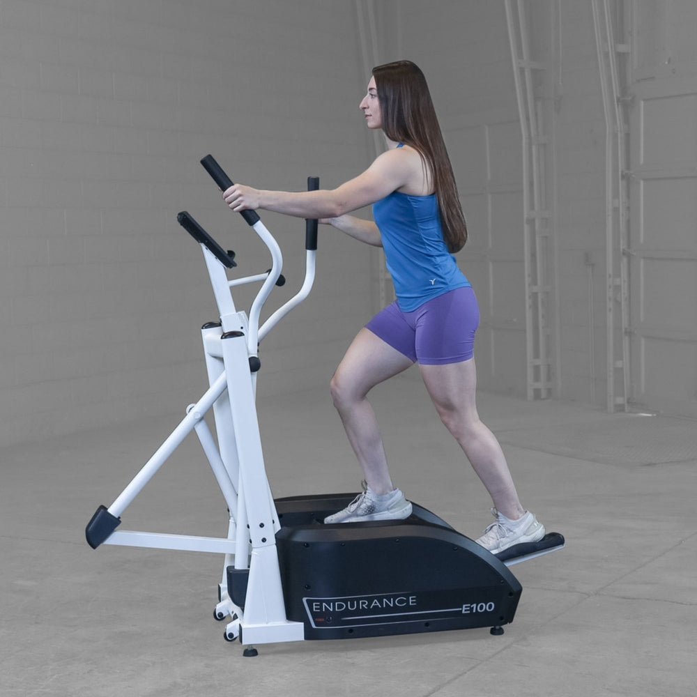 Body-Solid Endurance Center Drive Elliptical E100 Side view of woman striding on Endurance E100 elliptical trainer, demonstrating smooth motion and posture alignment.