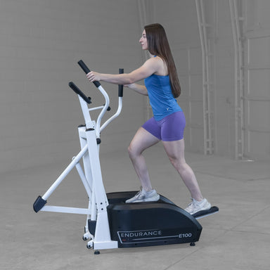 Body-Solid Endurance Center Drive Elliptical E100 Side view of woman striding on Endurance E100 elliptical trainer, demonstrating smooth motion and posture alignment.