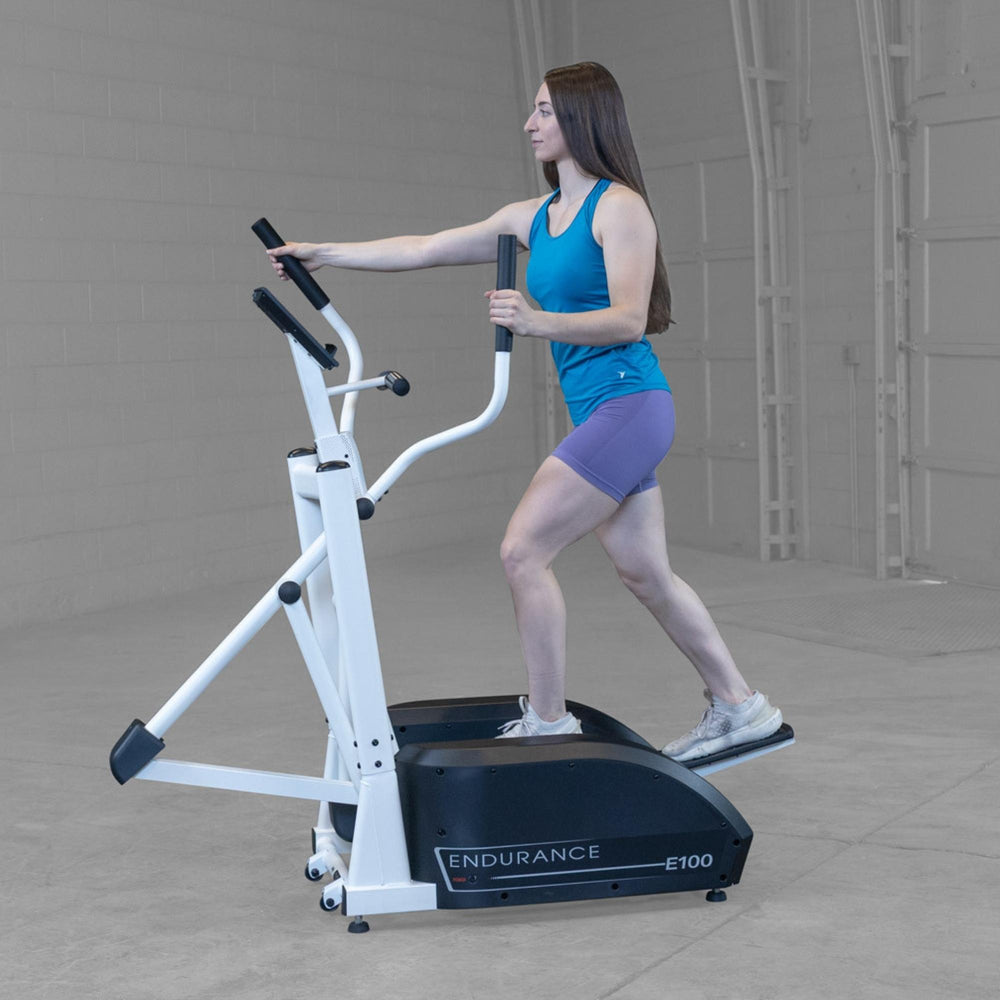 Body-Solid Endurance Center Drive Elliptical E100 Woman performing elliptical training on Endurance E100 machine, demonstrating ergonomic stride and handle use.
