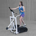 Body-Solid Endurance Center Drive Elliptical E100 Woman using Endurance E100 elliptical trainer, side view showing stride and full upper-body engagement.


