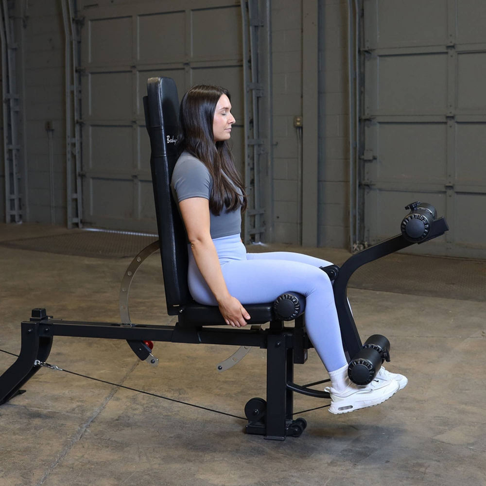 Body-Solid Leg Extension Curl Bench Attachment GLEG Woman performing seated leg extension exercise using Body-Solid bench leg developer attachment.