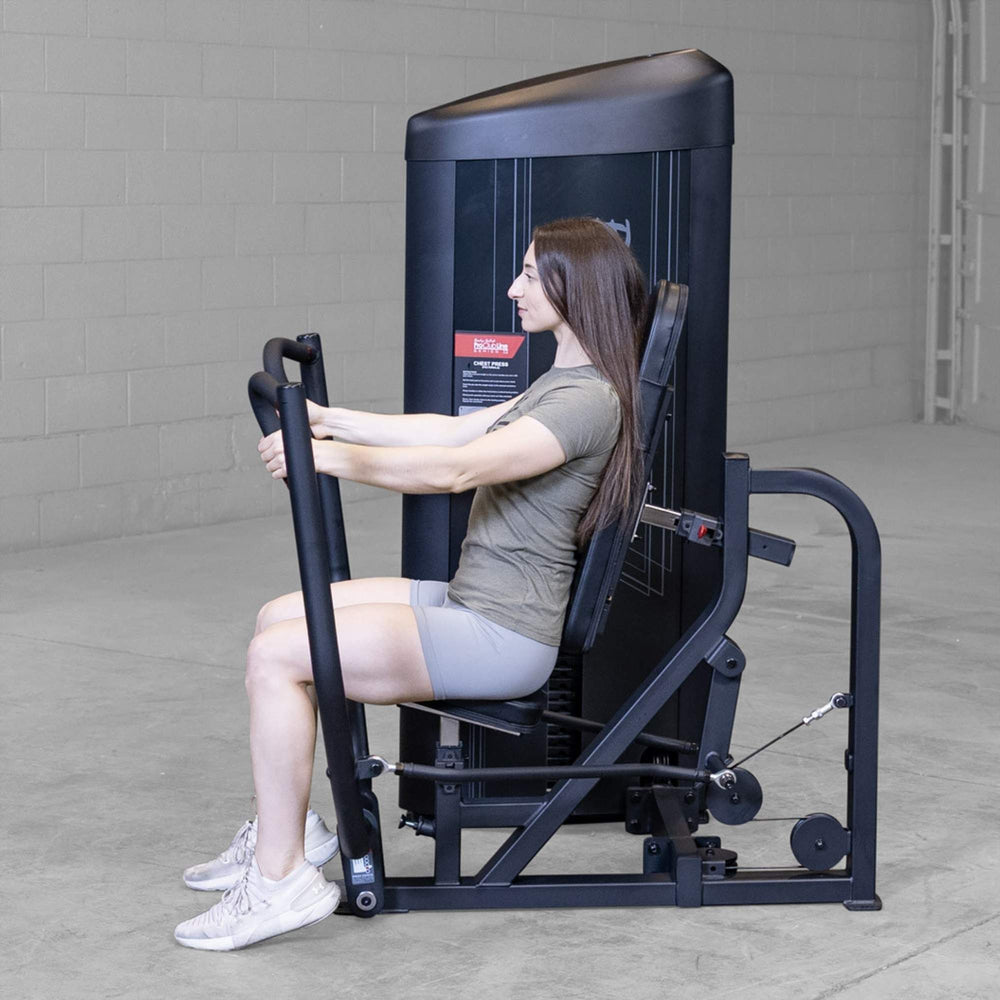 Body-Solid PCL2 Chest Press S2CPX Side view of a woman using a Body-Solid Pro Club Line chest press machine, seated upright and pushing the handles forward.