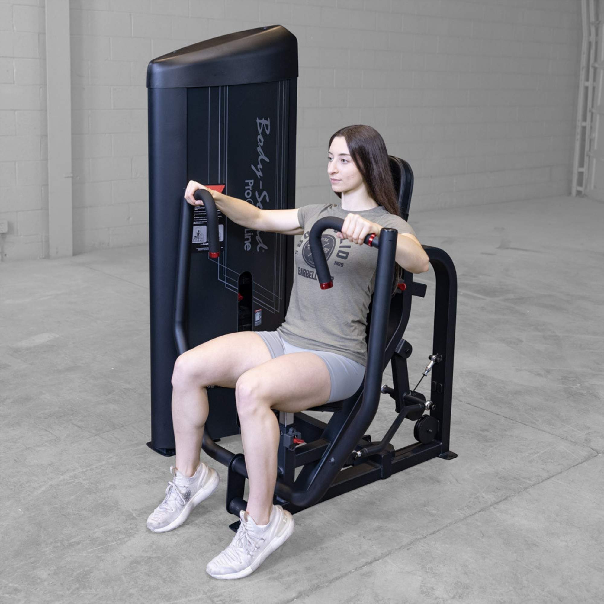 Body-Solid PCL2 Chest Press S2CPX Woman performing a chest press on a Body-Solid Pro Club Line machine, arms extended forward, seated in a workout area