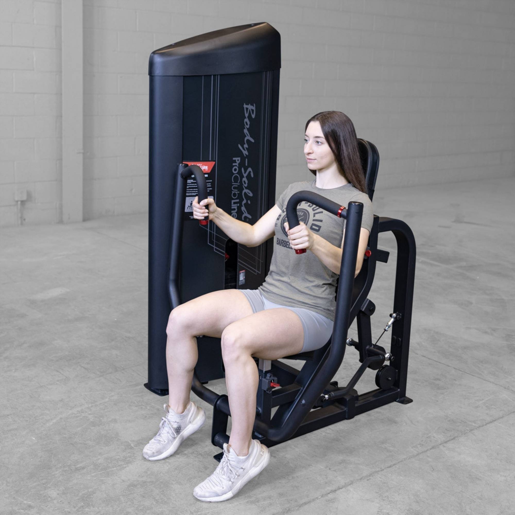 Body-Solid PCL2 Chest Press S2CPX Woman using a Body-Solid Pro Club Line chest press machine, seated and pushing the handles forward in a gym setting