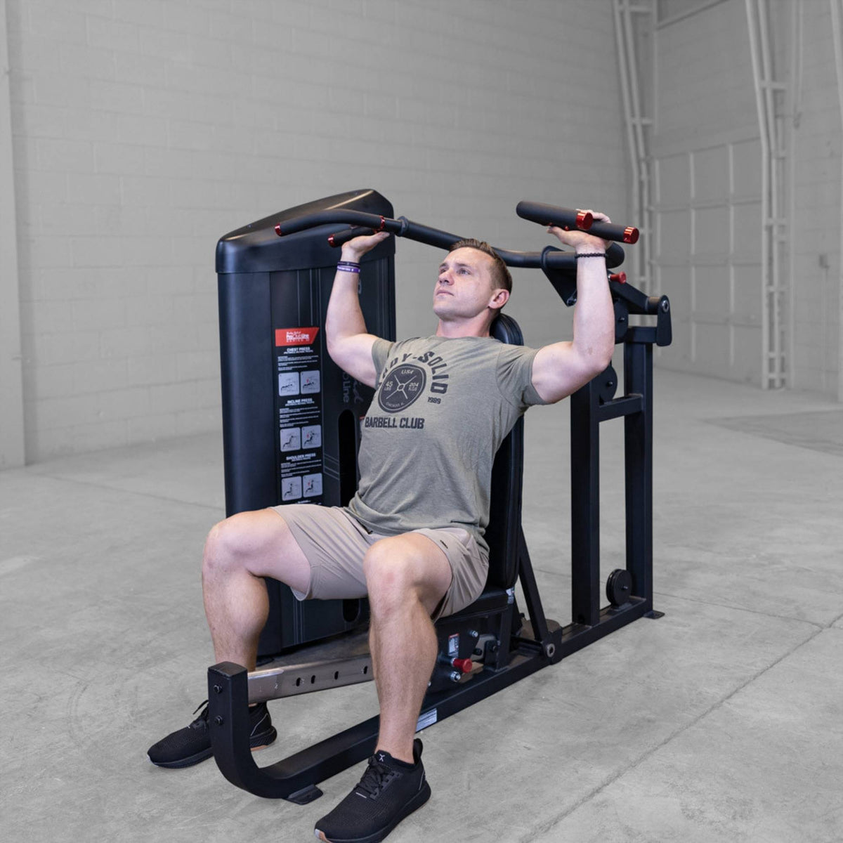 Body-Solid PCL2 Multi Press S2MPX Man seated pressing overhead on the machine while wearing a gray shirt