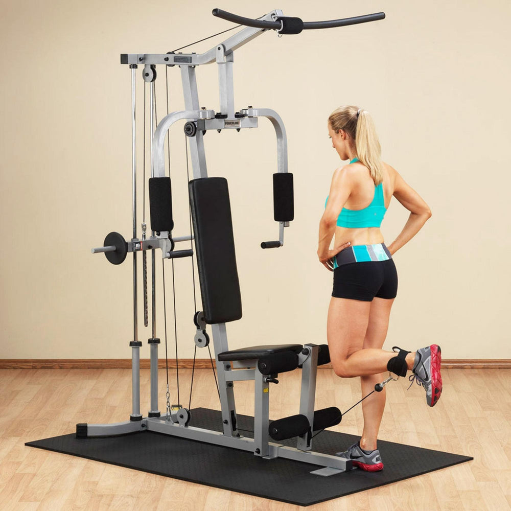 Body-Solid Powerline Plate Load Multi-Station Gym PHG1000X Woman using ankle strap attachment for standing leg curl exercise