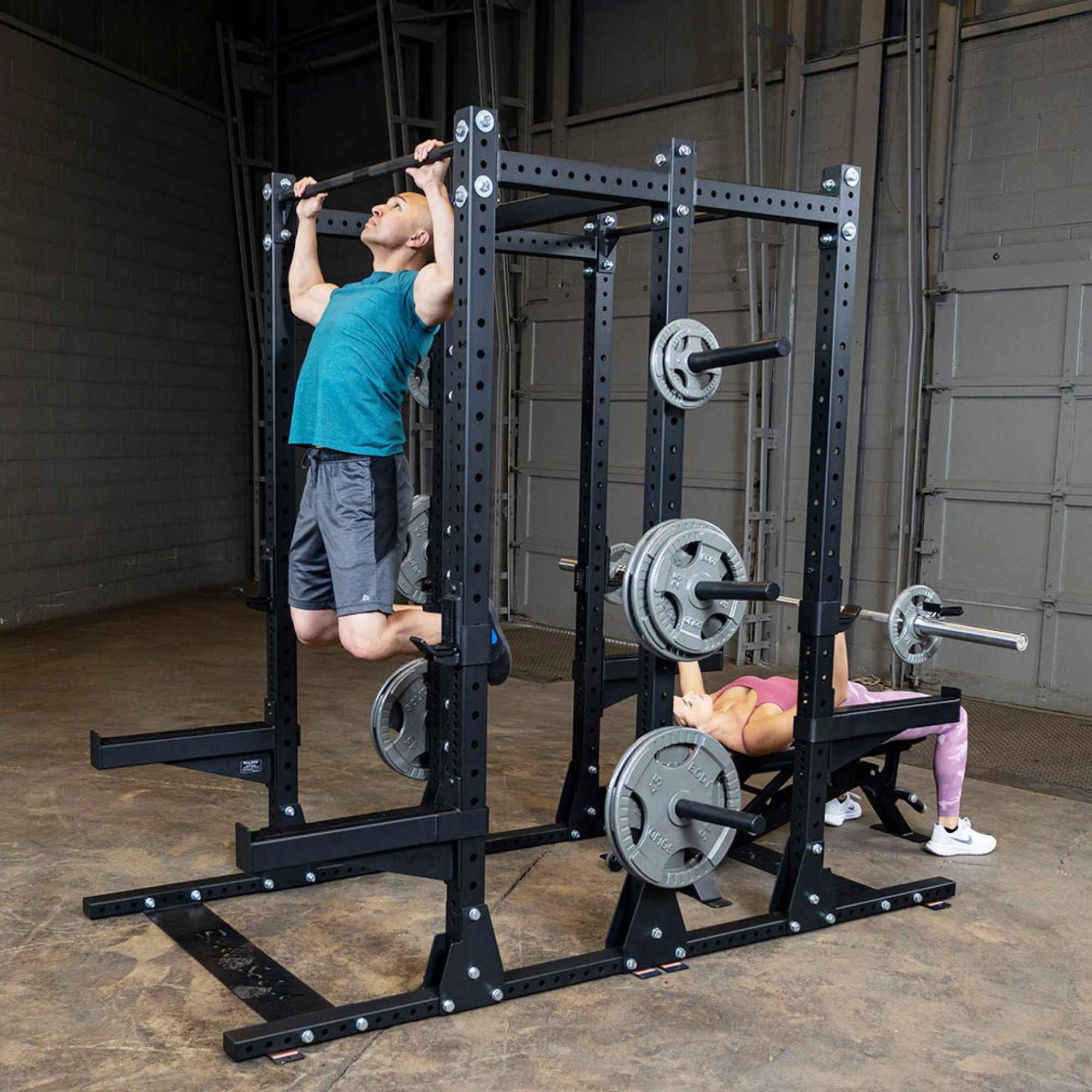 Body-Solid Pro ClubLine Double Half Rack SPR500DBL Dual training view — woman bench pressing and man squatting on Body-Solid SPR500DBL half rack system with loaded Olympic bars.
