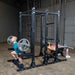 Body-Solid Pro ClubLine Double Half Rack SPR500DBL Man performing barbell squat and woman bench pressing on Body-Solid SPR500DBL power rack in industrial gym environment.
