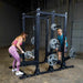 Body-Solid Pro ClubLine Double Half Rack SPR500DBL Woman doing bent-over barbell row while man prepares for deadlift beside Body-Solid SPR500DBL rack with weight plates loaded.
