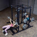 Body-Solid Pro ClubLine Double Half Rack SPR500DBL Woman performing bench press and man performing barbell squat simultaneously on Body-Solid SPR500DBL Double Half Rack in gym setting.
