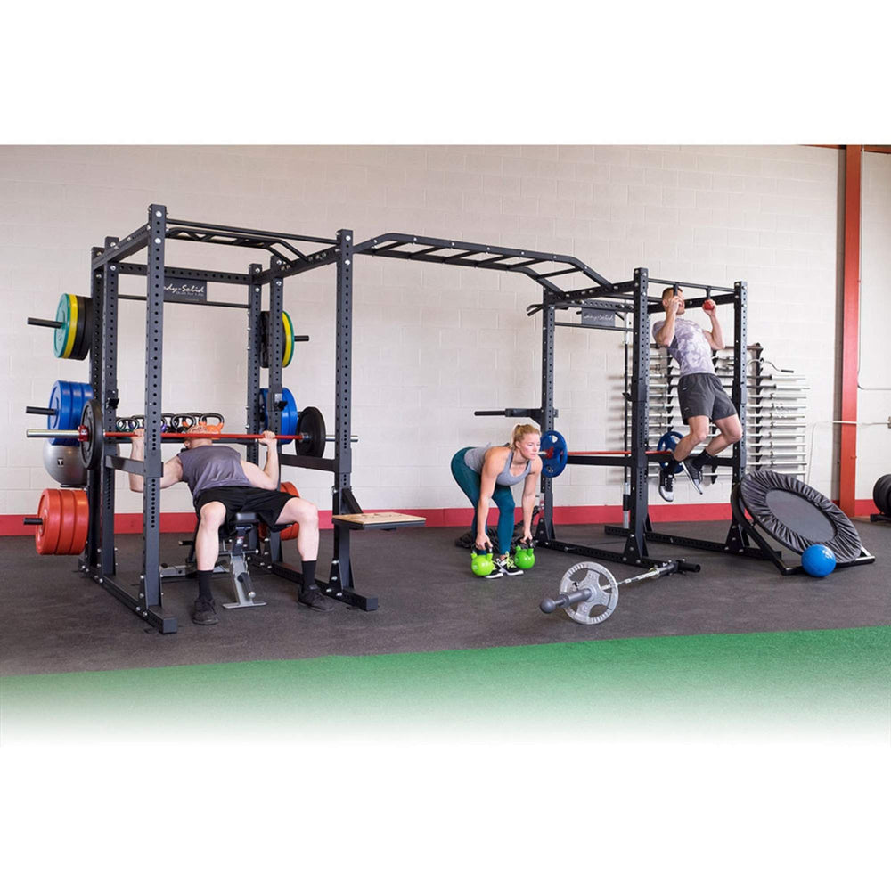 Body-Solid Pro ClubLine Double Power Racks with Monkey Bars and Safety Straps SPR1000SSDB A group of 3 people exercising on a large, multi-station black fitness rig in a gym
