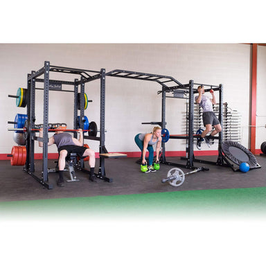 Body-Solid Pro ClubLine Double Power Racks with Monkey Bars and Safety Straps SPR1000SSDB A group of 3 people exercising on a large, multi-station black fitness rig in a gym