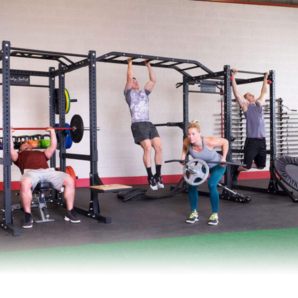 Body-Solid Pro ClubLine Double Power Racks with Rear Extensions and Monkey Bars SPR1000DBBACK  A group of four people exercising on a large, multi-station black fitness rig in a gym. On the left, a man is bench pressing. 